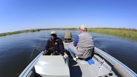 A-stern-view-of-a-tiger-fishing-boat-with-2-people-on-it-fishing-along-one-of-the-side-channels-on-the-Chobe-river