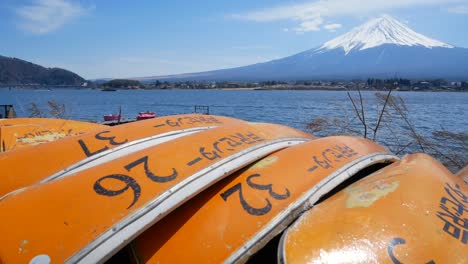 Blick-Auf-Den-Vulkan-Fuji-Mit-Dem-Kawaguchi-See-Und-Einer-Orangefarbenen-Gruppe-Kleiner-Kanus-In-Ufernähe-An-Einem-Frühlingstag-Mit-Klarem-Himmel-–-4K-UHD-Videofilmmaterial,-Kurz