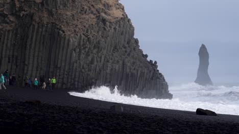 Tourists-running-away-from-waves-on-the-black-sand-beach-in-south-Iceland,-slow-motion-handheld-video