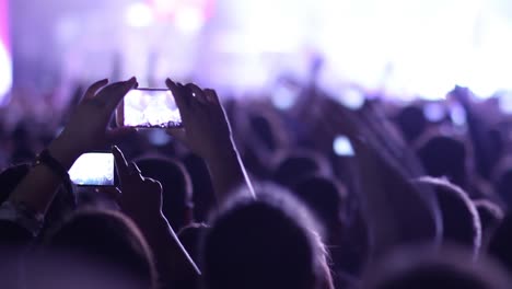 People-at-music-rock-concert-taking-photos-or-recording-video-with-smartphones,-party-crowd-cheering-at-music-event-with-flashing-light-show