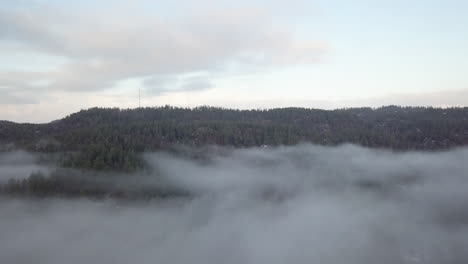 Aerial,-drone-shot,-over-a-thick-fog,-towards-a-hill,-full-of-frosty-forest-and-hills,-on-a-freezing-foggy,-autumn-morning,-in-Birkeland,-Aust-Agder,-South-Norway