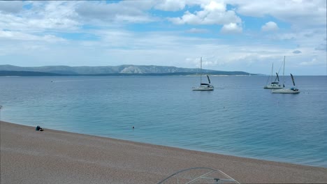 A-small-boat-filled-with-people-going-behind-a-sailboat-at-Zlatni-Rat-beach,-Croatia
