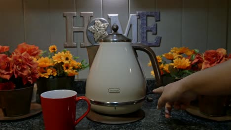 Hand-switching-kettle-button-on-next-to-mug-on-kitchen-counter,-static