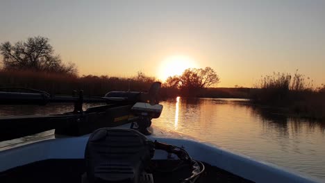 Bass-boat-moving-slowly-through-a-beautiful-river-with-the-sun-setting-in-the-distance