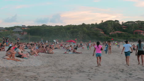 Große-Menge-Junger-Reisender,-Die-Im-Sand-Am-Strand-Sitzen-Und-Entspannen-Und-Den-Sonnenuntergang-In-Mexiko-Beobachten---Zeitlupe