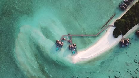 Aerial,-screwdriver,-drone-shot,-rising-above-a-white-sand-beach-and-bungalows-on-water,-at-a-turquoise-lagoon,-on-a-sunny-day,-on-the-Conrad-Rangali-island,-in-Maldives