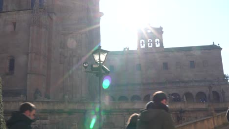 Salamanca,-Spain---December-7,-2019:-Tourists-head-towards-Salamanca-cathedral-up-a-hill,-the-cathedral-with-the-sun-flare-in-the-background