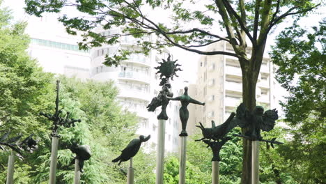 Statues-of-Japanese-mythical-creatures-sit-amongst-nature-in-a-peaceful-Tokyo-park-with-modern-apartment-blocks-in-the-background