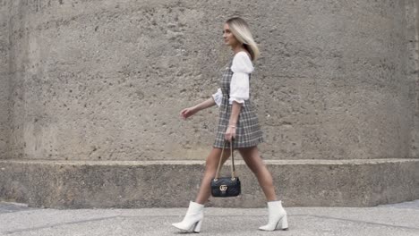 Wide-shot-of-blonde-women-walking-past-wall-in-slow-motion-holding-a-Gucci-bag