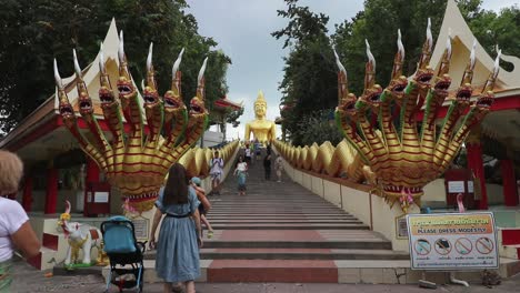 Turistas-Subiendo-Las-Escaleras-Del-Dragón-Dorado-Mientras-Visitan-La-Estatua-Del-Gran-Buda-En-Pattaya,-También-Conocida-Como-Wat-Phra-Yai,-Tailandia