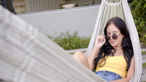 A-young-biracial-woman-lounges-in-hammock-with-sunglasses-on,-copy-space