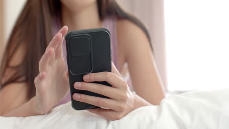 Teenage-Caucasian-girl-with-brown-hair-is-using-a-smartphone-in-bed-at-home