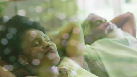 Animation-of-light-spots-over-african-american-couple-relaxing,-slow-motion