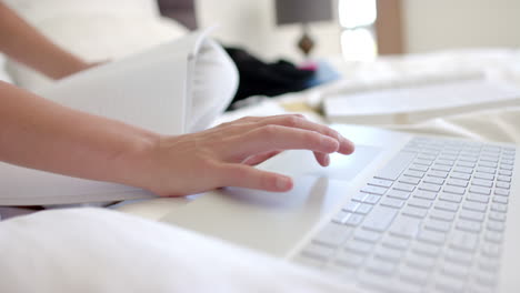 Close-up-of-a-teenage-girl''s-hands-typing-on-a-laptop-with-a-notebook-beside-them-at-home