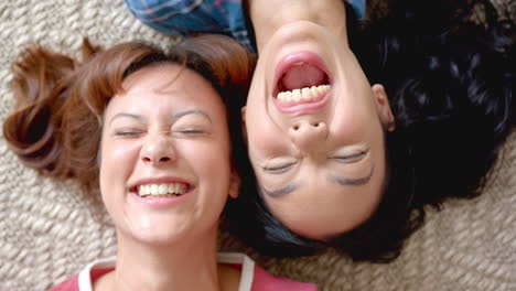Two-young-biracial-female-friends-are-lying-down,-heads-together,-sharing-a-joyful-moment