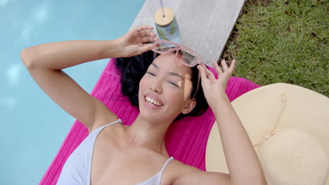 A-young-biracial-woman-lies-on-a-pink-pool-float,-smiling-with-her-eyes-closed