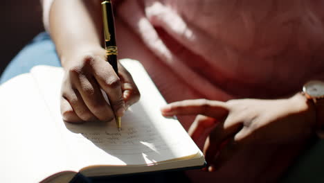 Close-up-of-an-African-American-woman-writing-in-a-notebook-at-home