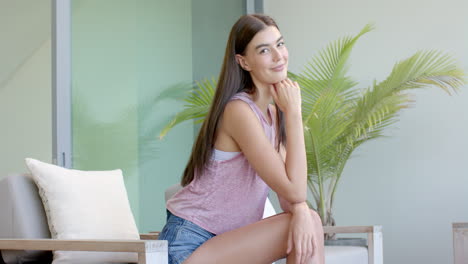 A-teenage-Caucasian-girl-with-long-brown-hair-and-a-sleeveless-top-is-smiling-at-home