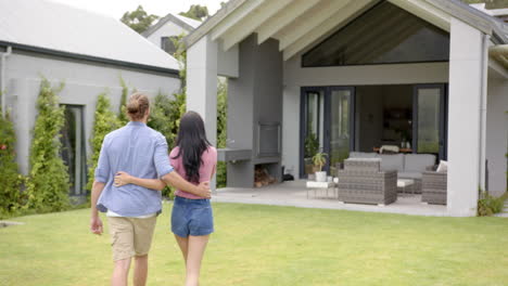 A-young-biracial-couple-stands-together-in-backyard,-looking-at-home,-copy-space