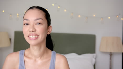 A-young-biracial-woman-with-her-hair-pulled-back-smiles-gently-in-a-bedroom,-with-copy-space