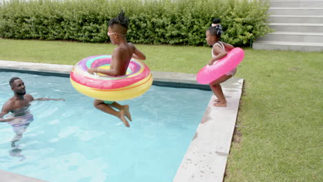 Glückliche-Familie-Aus-Einem-Afroamerikanischen-Mann-Und-Einem-Jungen,-Die-Zu-Hause-In-Einem-Pool-Spielen,-Während-Ein-Mädchen-Hineinspringt