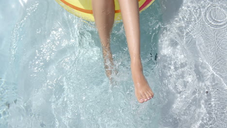 Close-up-of-a-young-woman''s-legs-dangling-in-a-pool-from-an-inflatable-ring