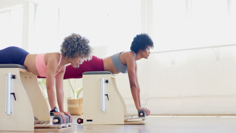 Two-biracial-women,-one-young-and-one-mature,-exercising-on-pilates-machines