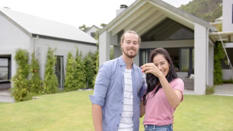 A-young-diverse-couple-is-smiling-outdoors-in-the-backyard-at-home,-holding-keys