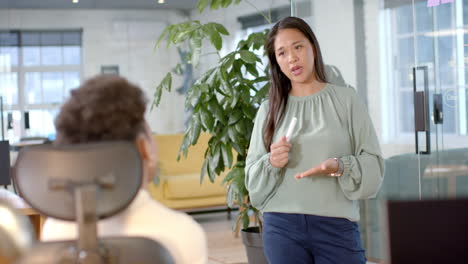 Asian-businesswoman-standing,-talking-to-African-American-colleague-seated