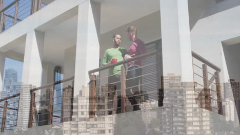 Animation-of-cityscape-over-diverse-male-couple-standing-on-balcony-and-drinking-coffee