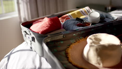 A-suitcase-lies-open-on-a-bed,-filled-with-clothes-and-a-straw-hat