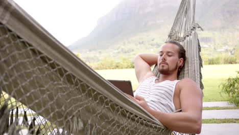 A-young-Caucasian-man-with-long-brown-hair-and-beard-relaxes-in-a-hammock