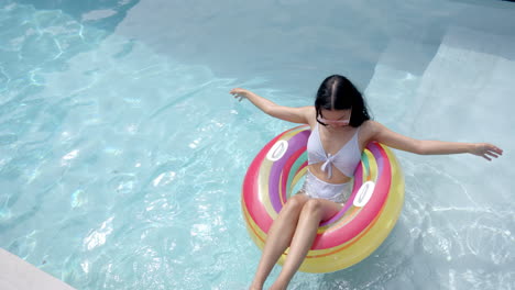 A-young-biracial-woman-lounges-on-a-colorful-pool-float