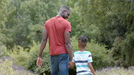 Padre-E-Hijo-Afroamericanos-Caminan-De-La-Mano-En-Un-Exuberante-Parque-En-Casa