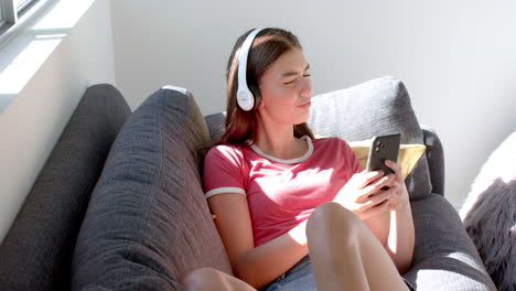 Una-Adolescente-Caucásica-Disfruta-De-La-Música-En-Sus-Auriculares-Mientras-Usa-Un-Teléfono-Inteligente-En-Casa