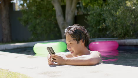 Asian-college-student-sitting-by-pool,-looking-at-smartphone
