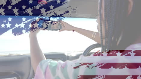 Animation-of-flag-of-usa-over-african-american-woman-in-car-by-beach-in-summer