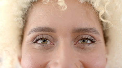 Close-up-of-a-young-biracial-woman''s-eyes,-framed-by-curly-blonde-hair,-at-home