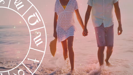 Animation-of-horoscope-moving-over-biracial-couple-holding-hands-at-beach