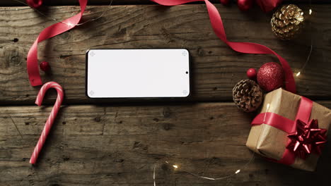 A-smartphone-with-a-blank-screen-lies-among-holiday-decorations-on-a-wooden-surface