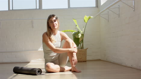 Caucasian-woman-sitting-on-floor-next-to-yoga-mat