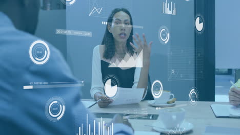 Animation-of-charts-processing-data-over-biracial-businesswoman-talking-at-casual-office-meeting