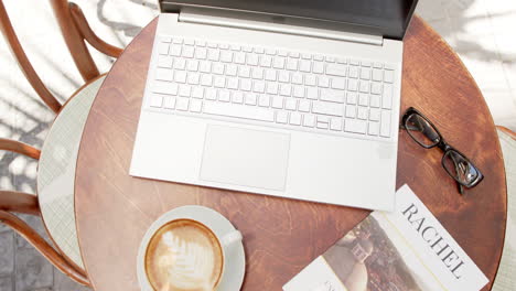 Ein-Laptop-Liegt-Geöffnet-Auf-Einem-Runden-Tisch-Neben-Einer-Tasse-Kaffee-Und-Einer-Brille-In-Einem-Café