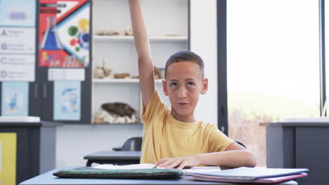 Biracial-boy-in-a-classroom-raises-his-hand,-eager-to-answer-a-question-in-school