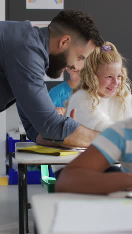 Vertical-video-of-happy-male-teacher-and-diverse-schoolchildren-in-school-classroom