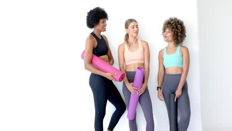 Three-women-are-standing-together,-holding-yoga-mats