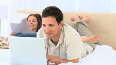 Happy-man-working-on-the-computer-while-his-wife-is-reading-a-book