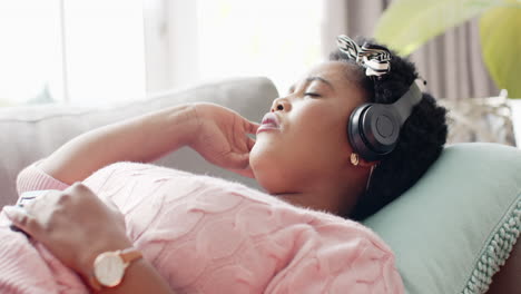 African-American-woman-relaxes-with-headphones-on-a-couch-at-home