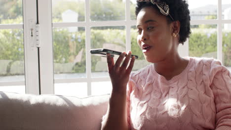 African-American-woman-speaks-into-a-phone,-sunlight-streams-in-at-home