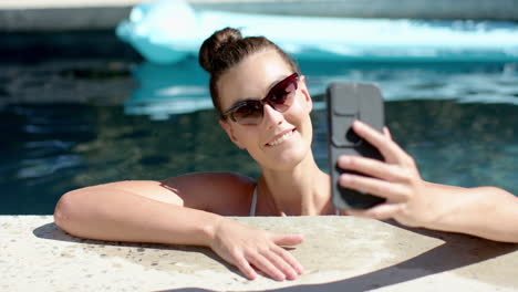 Teenage-girl-with-sunglasses-takes-a-selfie-by-the-pool,-puckering-her-lips-for-the-camera